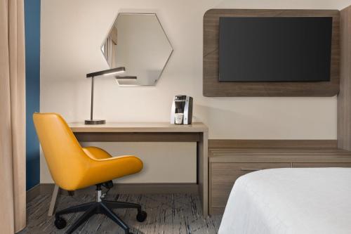 a bedroom with a desk with a yellow chair and a tv at Holiday Inn Express & Suites Greenville-Downtown by IHG in Greenville