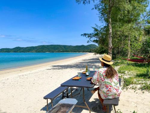 a woman sitting at a picnic table on the beach at Le Grand Bleu in Amami