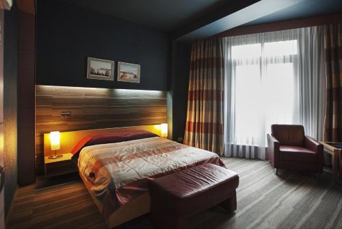 a bedroom with a bed and a chair and a window at Victoria Hotel & Business centre Minsk in Minsk