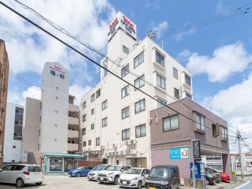 een hoog wit gebouw met auto's geparkeerd op een parkeerplaats bij Tabist Rays Hotel Yakata in Miyazaki