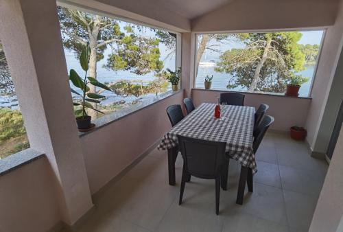 a dining room with a table and chairs and windows at Apartments by the sea Ugljan - 19580 in Ugljan