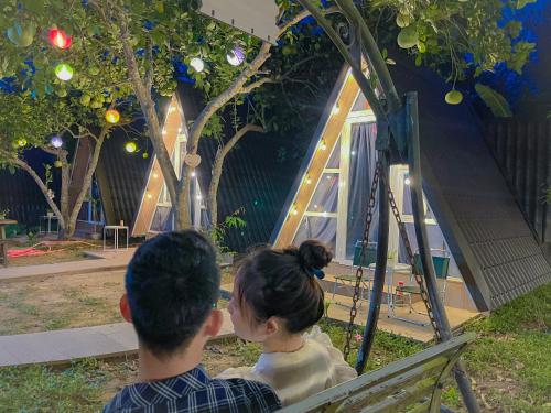 Ein Mann und eine Frau sitzen auf einer Bank und sehen ein Spielhaus an. in der Unterkunft Tam Tinh Vien Homestay in Hue