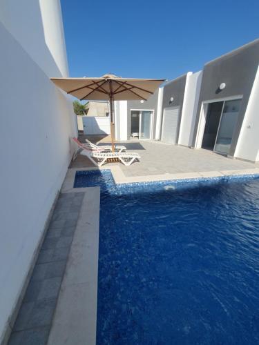una piscina con ombrellone e sedie accanto a un edificio di Villa de luxe avec piscine sans vis à vis Midoun ad Aghīr
