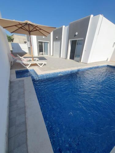 a swimming pool with an umbrella and a house at Villa de luxe avec piscine sans vis à vis Midoun in Aghīr
