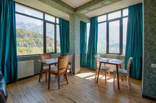 a room with tables and chairs and large windows at Hotel GENI Kazbegi in Stepantsminda