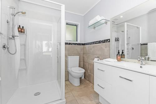 a white bathroom with a shower and a toilet at Sea View Cottage - Ruakaka Holiday Cottage in Ruakaka