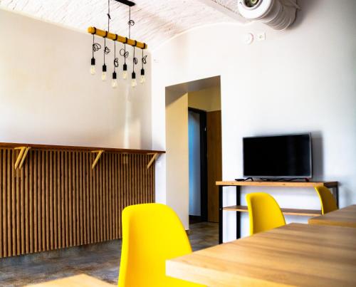 a dining room with yellow chairs and a table and a tv at FOKA Hostel in Wrocław