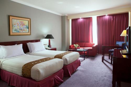 two beds in a hotel room with red curtains at Surabaya Suites Hotel Powered by Archipelago in Surabaya