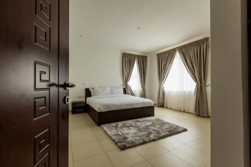 a bedroom with a bed and two windows and a door at Accra Fine Suites - Henrietta's Residences in Accra