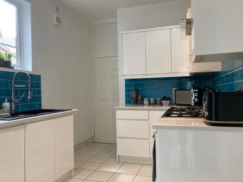 a kitchen with white cabinets and blue tiles at Tynwald Beachside Town House, West Kirby by Rework Accommodation in West Kirby
