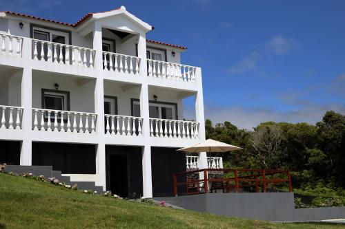un grande edificio bianco con balcone e ombrellone di Villa Capelinhos a Capelo