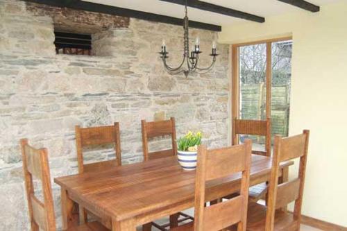 a dining room table with chairs and a stone wall at Tuell Farm Cottages in Tavistock