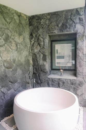 a bathroom with a white tub and a stone wall at Zenubud in Ubud