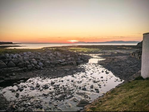 a sunset over a river with rocks and the ocean at Luxury 3 bedroom house with peaceful garden, sleeps 6 and 2 mins to beach in Bundoran