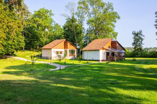 two small buildings in a grassy field with trees at Folwark Wierzchy in Wierzchy