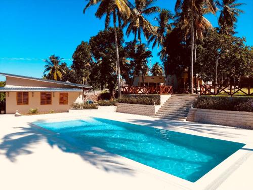 a swimming pool in front of a house with palm trees at Dive Planet Mafia Island in Utende