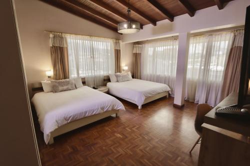 a bedroom with two beds with white sheets and windows at Hotel Sandmelis in Quito