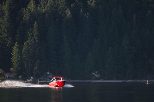 a red boat in the water near a forest at Tranquility Bay Waterfront Inn in Sechelt
