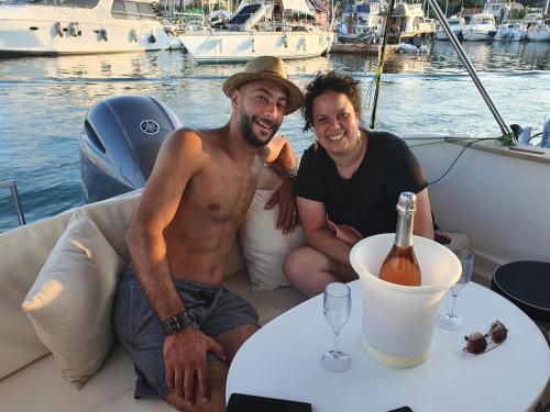 dwóch mężczyzn siedzących na łodzi ze stołem i butelką wina w obiekcie Nuit Insolite sur un Bateau w mieście Saint-Florent