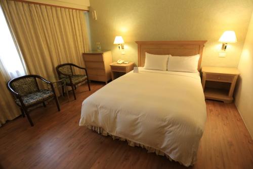 a hotel room with a large white bed and two chairs at Cambridge Tainan Hotel in Tainan