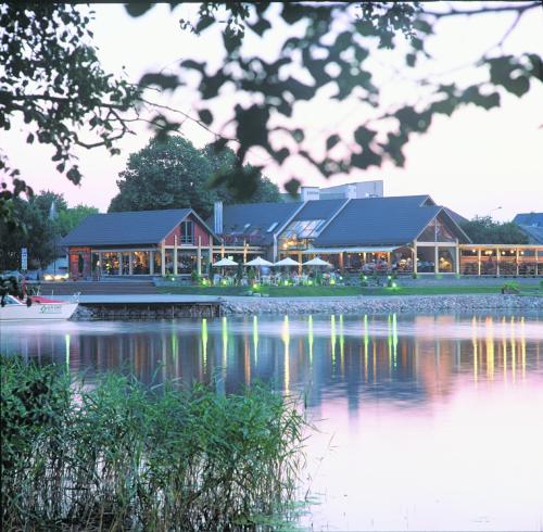 a building next to a lake with a boat at Apvalaus Stalo Klubas Gastro & SPA Hotel in Trakai