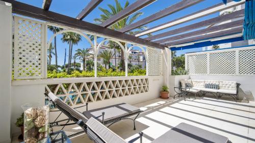 a balcony with chairs and tables and palm trees at Apartamento de 2 dormitorios en Las Gaviotas - Puerto Banús in Marbella