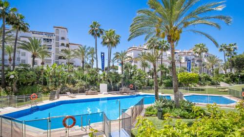 a swimming pool with palm trees and buildings at Apartamento de 2 dormitorios en Las Gaviotas - Puerto Banús in Marbella