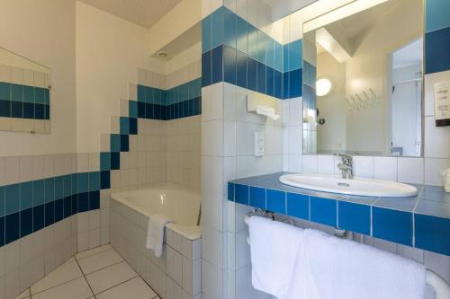 uma casa de banho com um lavatório, uma banheira e um espelho. em Abor Hôtel, Mont de Marsan em Saint-Pierre-du-Mont