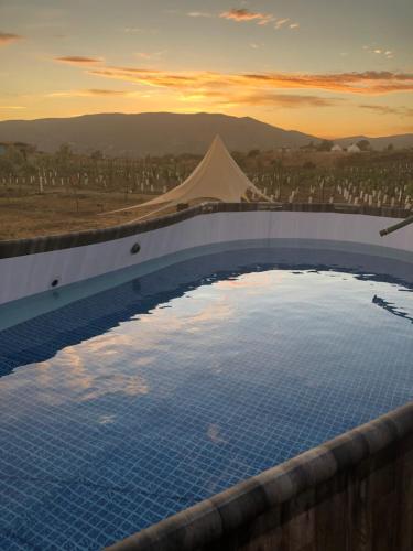 a large swimming pool with a sunset in the background at Lago Valle Wine Glamping in Valle de Guadalupe