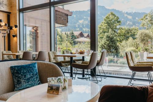 restauracja ze stołami i krzesłami oraz dużym oknem w obiekcie ERMITAGE Wellness- & Spa-Hotel w mieście Gstaad