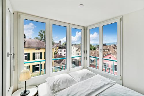 a bedroom with large windows and a bed with white sheets at Spacious Central Apartments HOTING in Zürich