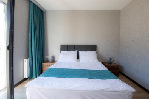 a bedroom with a large white bed with green curtains at Hotel GENI Kazbegi in Stepantsminda
