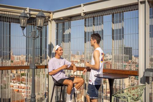 Dos hombres sentados en un balcón con vistas a la ciudad en Urbany Hostel Barcelona, en Barcelona