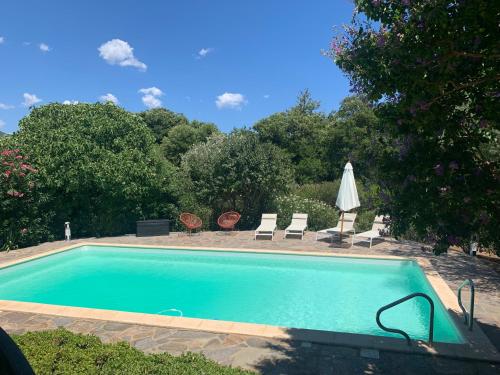 a swimming pool with two chairs and a umbrella at Villa dans un cadre verdoyant , piscine et jardin in Porto-Vecchio