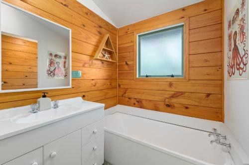 La salle de bains est pourvue d'un lavabo blanc et d'une baignoire. dans l'établissement Seaview, Sun and Surf - Piha Holiday Home, à Piha
