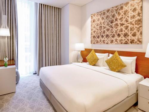 a bedroom with a large white bed with yellow pillows at Grand Mercure Hotel and Residences Dubai Airport in Dubai