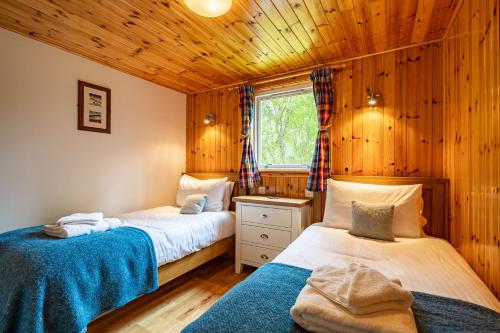 Duas camas num quarto com paredes de madeira e uma janela em Bracken Lodge 7 with Hot Tub em Belladrum