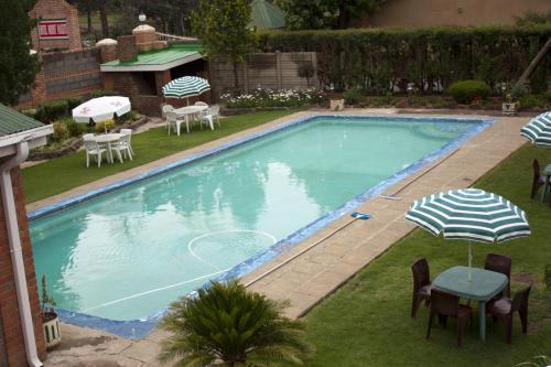 a swimming pool with a table and chairs and an umbrella at Hotel Mount Maluti - Lesotho in Mohales Hoek