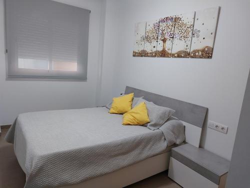 uma cama com almofadas amarelas num quarto branco em Piles residencial Blaumar del 1 al 10 de julio em Piles