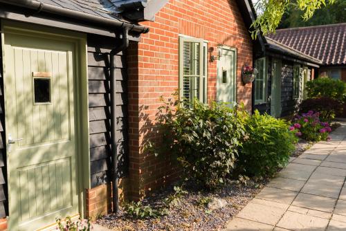 een bakstenen huis met een groene deur en ramen bij The Foxes Den in Assington