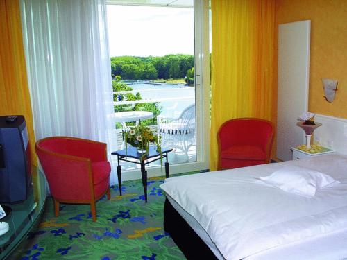 1 Schlafzimmer mit einem Bett, 2 Stühlen und einem Fenster in der Unterkunft Vitalia Seehotel in Bad Segeberg
