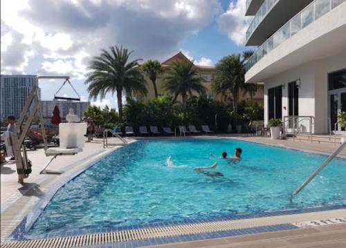 two people swimming in a large swimming pool at Beachy Vibes Studio, 2 Full Beds, Near Everything -30B in Hallandale Beach