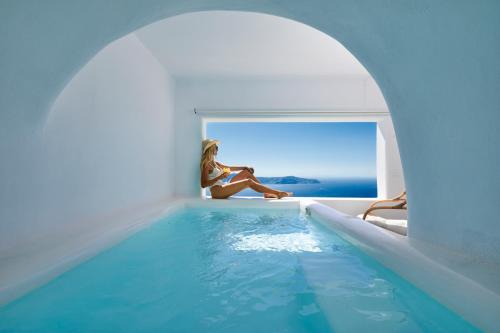 a woman sitting on a window sill next to a swimming pool at U & ME SUITES in Fira