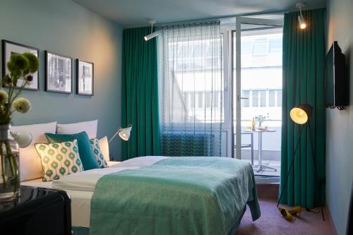 Schlafzimmer mit einem Bett mit grünen Vorhängen und einem Fenster in der Unterkunft Hotel Metropol by Maier Privathotels in München