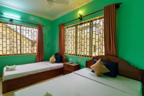 シェムリアップにあるHappy Heng Heang Guesthouseの緑の壁と窓が特徴の客室で、ベッド2台が備わります。