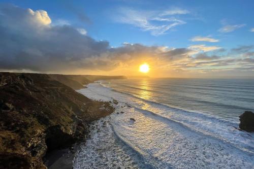 a sunset over a beach with the sun setting at Rosebud in Portreath