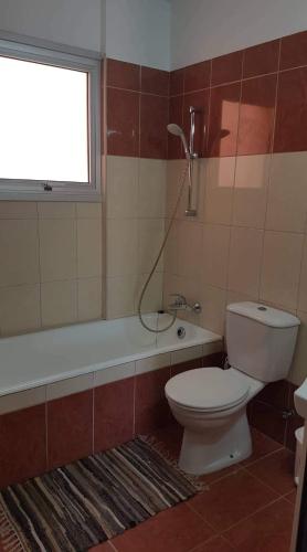 a bathroom with a toilet and a tub and a window at Andris apartment in Paralimni