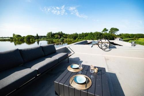 um pátio com um sofá, uma mesa e água em Surla houseboat "Aqua Zen" Kagerplassen with tender em Kaag