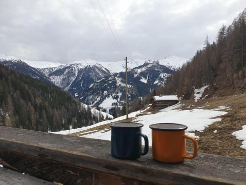 two coffee mugs sitting on a ledge overlooking a snowy mountain at Thaletalm in Innervillgraten