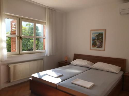 a bedroom with a large bed with two windows at Apartments Ruža Mikelić in Rab